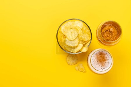 Téléchargez les photos : Une collation tentante de bière et de chips sur un fond jaune vif avec espace de copie. Pose plate - en image libre de droit