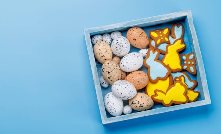Photo for Easter delights: Colorful eggs and gingerbread cookies in a box. Flat lay with copy space - Royalty Free Image
