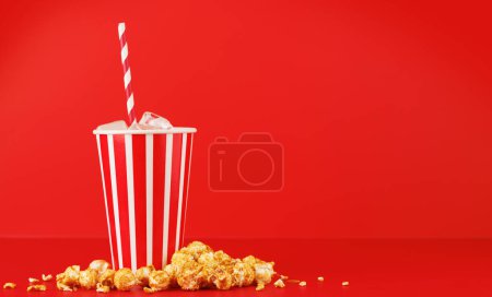 Paper cup with cola and ice and popcorn over red background, with copy space