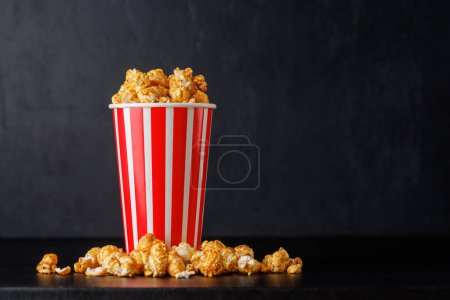 Popcorn in paper cup over black background with copy space