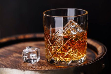 Téléchargez les photos : Verre à whisky avec glace sur un tonneau rustique, une gorgée classique. Avec espace de copie - en image libre de droit