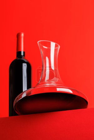 Red wine elegance: Decanter and wine bottle against a vibrant red background. With copy space