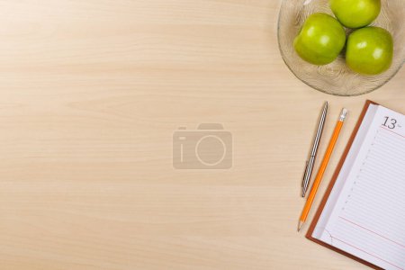 Foto de Aspectos esenciales del lugar de trabajo: manzanas, bloc de notas y suministros. Piso con espacio de copia - Imagen libre de derechos