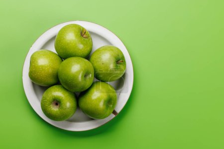 Photo for Plate with fresh green apples over green background. Flat lay with copy space - Royalty Free Image