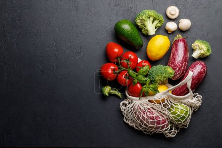 Photo for Mesh bag filled with a variety of vegetables. Flat lay over dark stone background with copy space - Royalty Free Image