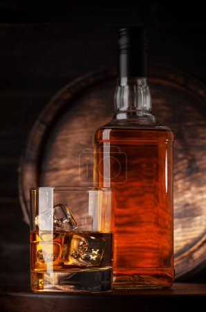 Photo for Glass and bottle with whiskey, cognac or golden rum. In front of old wooden barrel - Royalty Free Image