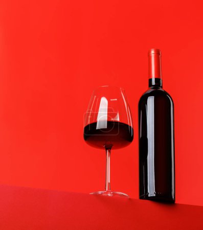 Red wine elegance: Wine glass and bottle against vibrant red background. With copy space