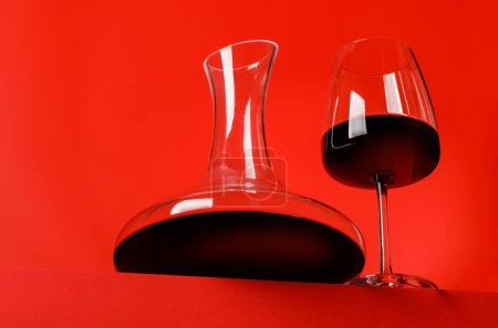 Rotweinelegantheit: Dekanter und Weinglas vor lebendigem roten Hintergrund. Mit Kopierraum