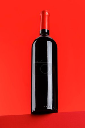 Photo for Red wine elegance: Wine bottle against vibrant red background. With copy space - Royalty Free Image