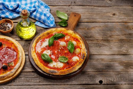 Foto de Pizza casera de margarita y pepperoni, cubierta con tomates frescos, queso mozzarella y hojas aromáticas de albahaca. En la mesa de jardín al aire libre con espacio de copia - Imagen libre de derechos