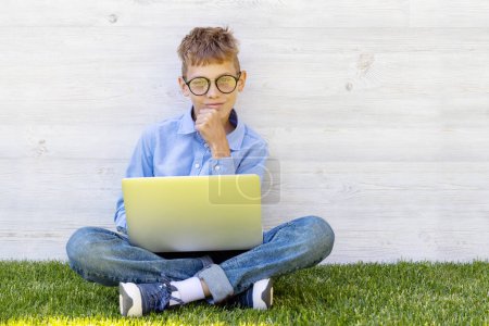 Téléchargez les photos : Un garçon qui utilise un ordinateur portable à l'extérieur. Concept d'éducation ou de divertissement - en image libre de droit