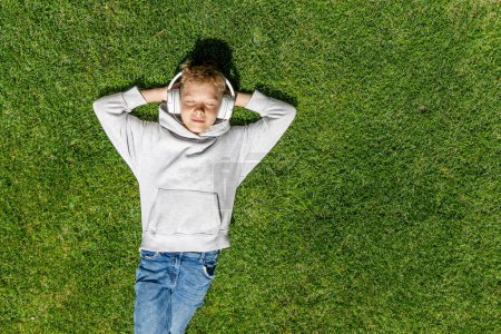 Foto de Un chico relajándose en la hierba, escuchando música con auriculares. Puesta plana - Imagen libre de derechos