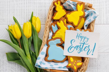 Photo for Easter Scene with Bunny-Shaped Gingerbread Cookies, Yellow Tulips, and Greeting card. Flat lay with copy space - Royalty Free Image
