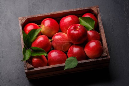 Wooden box with fresh red apples on stone table