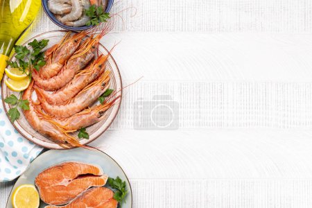 A top view of fresh seafood such as shrimp, langoustines, and trout steaks, accompanied by white wine. Flat lay with copy space