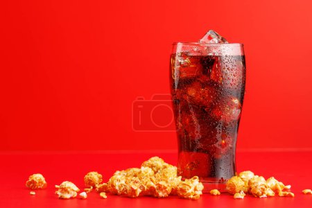 Cola con hielo y palomitas de maíz sobre fondo rojo, con espacio para copiar
