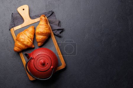 Téléchargez les photos : Théière et croissants frais sur table en pierre. Pose plate avec espace de copie - en image libre de droit