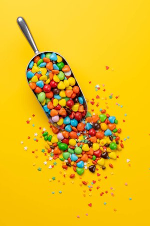 Various colorful candies in scoop. Flat lay over yellow background