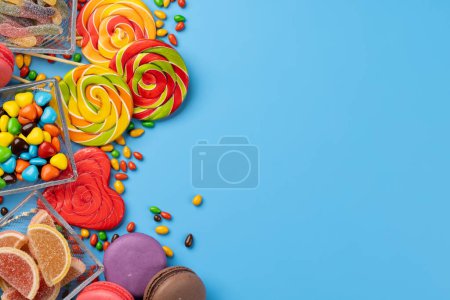 Foto de Varios caramelos coloridos, piruletas y macarrones. Dulces planos sobre fondo azul con espacio para copiar - Imagen libre de derechos