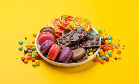 Téléchargez les photos : Divers bonbons colorés, sucettes et macarons. Sur fond jaune - en image libre de droit