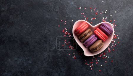 Téléchargez les photos : Divers macarons colorés dans un bol en forme de coeur. Amour bonbons sur fond de pierre avec espace de copie - en image libre de droit