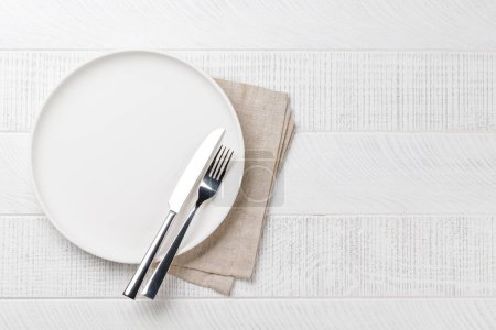 Empty plate, fork and knife on wooden table, overhead view with copy space