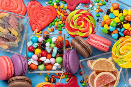 Foto de Varios caramelos coloridos, piruletas y macarrones. Flat lay dulces sobre fondo azul - Imagen libre de derechos