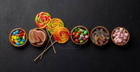 Various colorful candies, lollipops, and macaroons. Flat lay over stone background with copy space