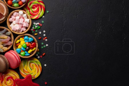 Various colorful candies, lollipops, and macaroons. Flat lay sweets over stone background with copy space