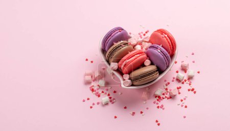 Téléchargez les photos : Divers macarons colorés dans un bol en forme de coeur. Bonbons amour sur fond rose avec espace de copie - en image libre de droit