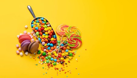 Foto de Varios caramelos coloridos, piruletas y macarrones. Sobre fondo amarillo con espacio de copia - Imagen libre de derechos