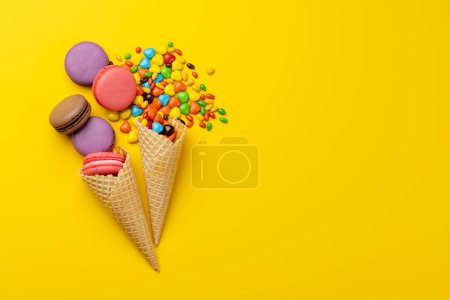 Téléchargez les photos : Divers bonbons colorés, sucettes et macarons. Poser des bonbons plats sur fond jaune avec espace de copie - en image libre de droit