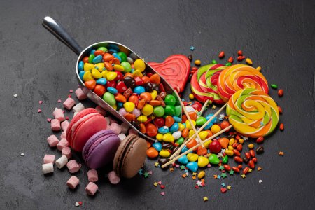 Téléchargez les photos : Divers bonbons colorés, sucettes et macarons. Bonbons sur fond de pierre - en image libre de droit