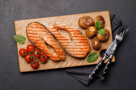 Grilled salmon steaks and potatoes on a wooden board, a mouthwatering delight. Flat lay