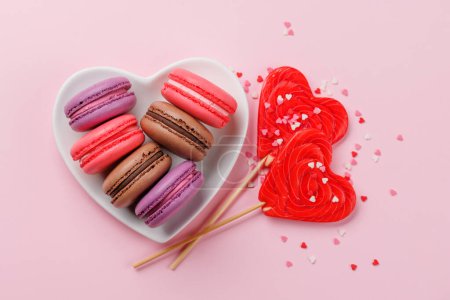 Téléchargez les photos : Divers macarons colorés dans un bol en forme de coeur. Bonbons d'amour sur fond rose - en image libre de droit