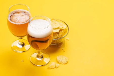 A tempting snack of beer and chips on a vibrant yellow background with copy space