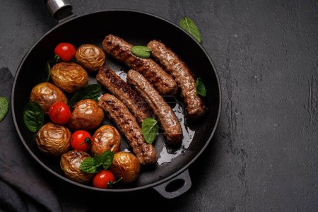 Téléchargez les photos : Délicieuses saucisses grillées et pommes de terre dans une poêle à frire pétillante avec espace de copie - en image libre de droit