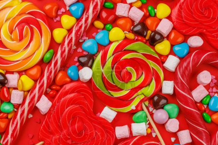 Foto de Varios caramelos coloridos, piruletas y macarrones. Piso sobre fondo rojo - Imagen libre de derechos