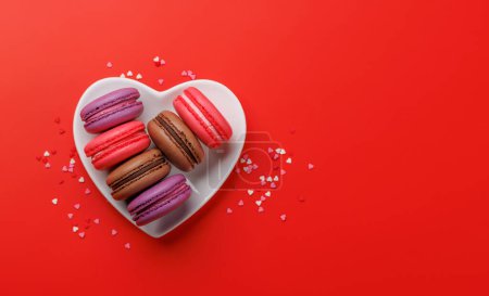 Téléchargez les photos : Divers macarons colorés dans un bol en forme de coeur. Amour bonbons sur fond rouge avec espace de copie - en image libre de droit