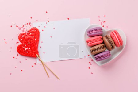 Téléchargez les photos : Divers macarons colorés dans un bol en forme de coeur. Bonbons amour sur fond rose avec carte de vœux - en image libre de droit
