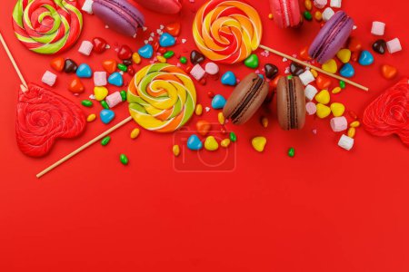Foto de Varios caramelos coloridos, piruletas y macarrones. Piso sobre fondo rojo con espacio de copia - Imagen libre de derechos