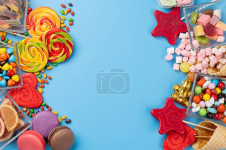 Varios caramelos coloridos, piruletas y macarrones. Dulces planos sobre fondo azul con espacio para copiar
