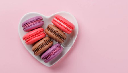 Photo for Various colorful macaroons in heart shaped bowl. Love sweets over pink background with copy space - Royalty Free Image