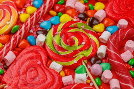 Foto de Varios caramelos coloridos, piruletas y macarrones. Sobre fondo rojo - Imagen libre de derechos