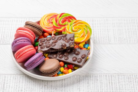 Téléchargez les photos : Divers bonbons colorés, sucettes et macarons. Sur fond en bois avec espace de copie - en image libre de droit