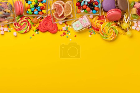 Foto de Varios caramelos coloridos, piruletas y macarrones. Piso sobre fondo amarillo con espacio de copia - Imagen libre de derechos