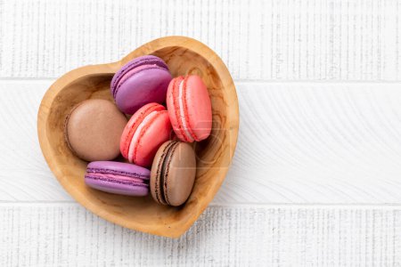 Téléchargez les photos : Divers macarons colorés dans un bol en forme de coeur. Amour bonbons sur fond en bois avec espace de copie - en image libre de droit