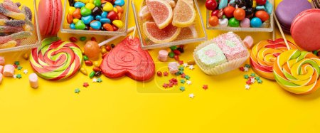 Téléchargez les photos : Divers bonbons colorés, sucettes et macarons. Sur fond jaune avec espace de copie - en image libre de droit
