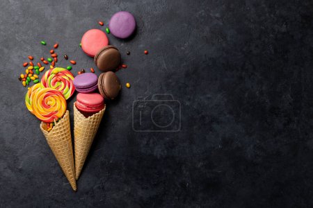 Foto de Varios caramelos coloridos, piruletas y macarrones. Dulces planos sobre fondo de piedra con espacio para copiar - Imagen libre de derechos