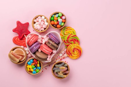 Varios caramelos coloridos, piruletas y macarrones. Piso sobre fondo rosa con espacio de copia